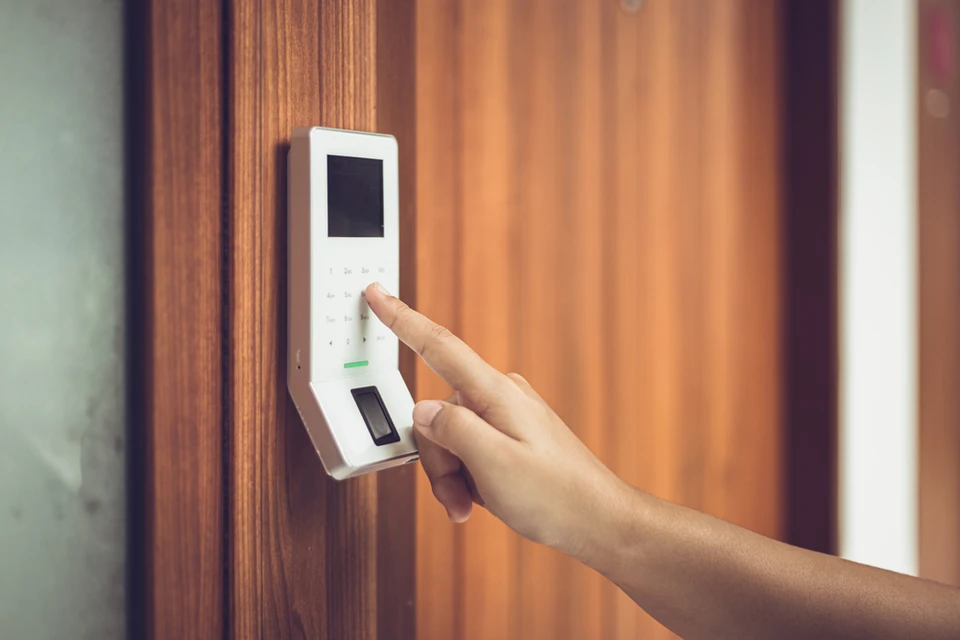 Une main utilise un système de contrôle d'accès biométrique à reconnaissance d'empreintes digitales, monté sur une porte en bois
