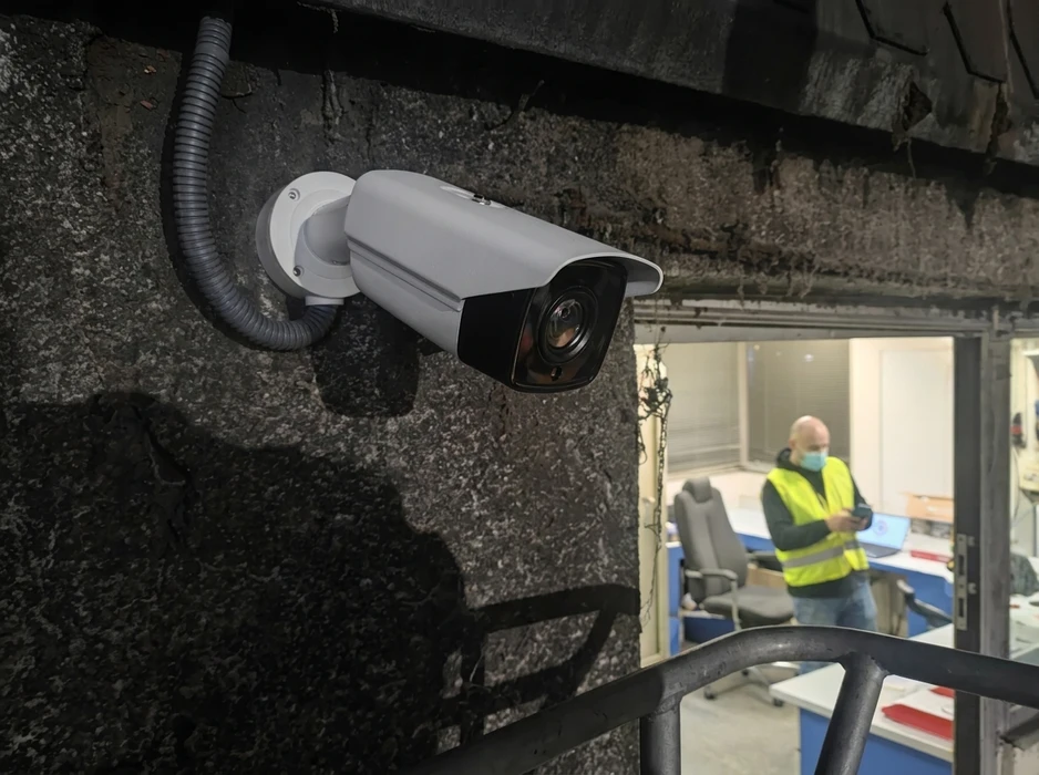 Technicien en gilet jaune et masque chirurgical dans un local industriel, consultant un appareil mobile