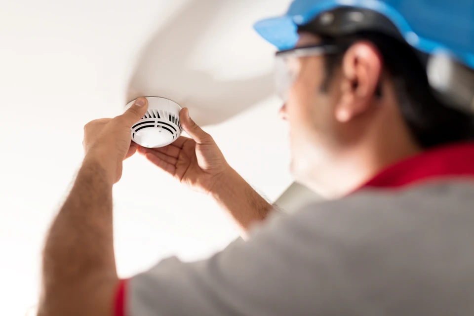 Un technicien installe un détecteur de fumée au plafond d'un intérieur résidentiel