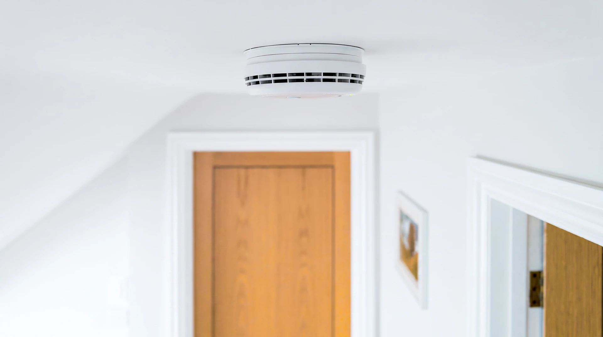 Intérieur d'un bâtiment commercial moderne (bureau, entrepôt ou établissement recevant du public). Au plafond, visible en gros plan, un détecteur de fumée blanc monté professionnellement. L'ambiance générale doit être calme, sécurisante et montrer un environnement bien aménagé. La perspective doit permettre de clairement visualiser l'équipement de détection incendie installé en tant que élément de sécurité intégré au bâtiment.